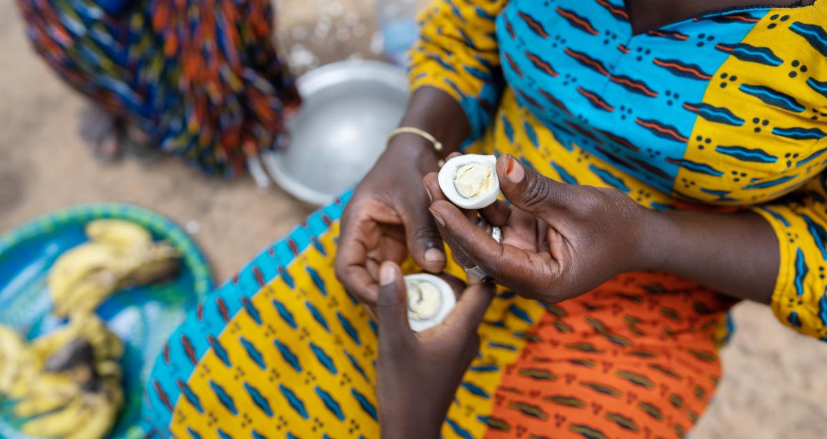 A woman from Bamako, Mali in a colorful dress sitting on the floor in a rural village kitchen, sharing half of an egg with a child in Bamako, Mali.  Photo credit Shutterstock/ By Riccardo Mayer