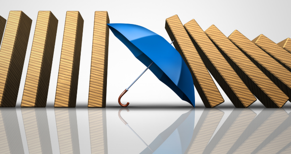 Protect losses concept and shielding incoming disaster as an umbrella stopping the domino effect or falling dominos as a business guarantee metaphor as a 3D illustration. Photo Credit: Shutterstock/Lightspring