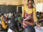 A teacher trainee helps out in the class two classroom by passing out textbooks. As part of her training she will spend three weeks observing and working with each teacher in the school. Sandogo “B” primary school, District 7, Ouagadougou.Credit: GPE Kelley Lynch
